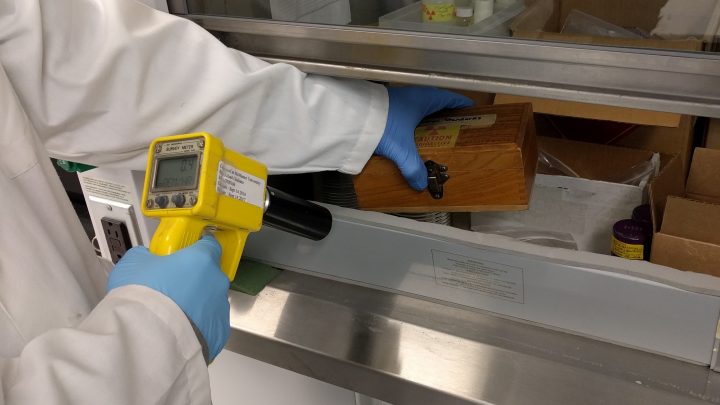 lab worker using a radiation surveying tool to measure radiation from radioactive materials
